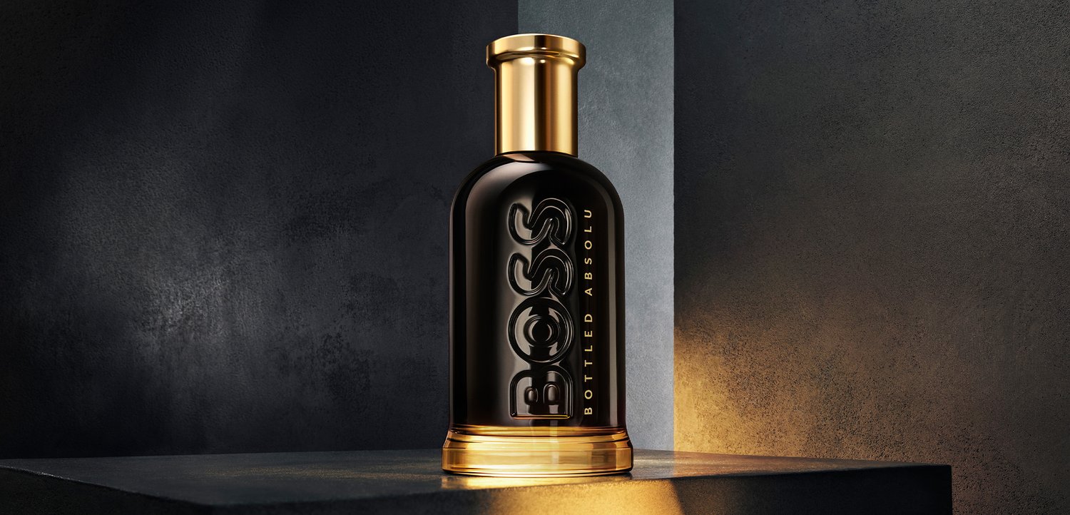 Schwarze und goldene Boss Bottled Absolut Kölnflasche auf einer dunklen Oberfläche mit warmem Licht, das ihren Boden und die Seite hervorhebt.