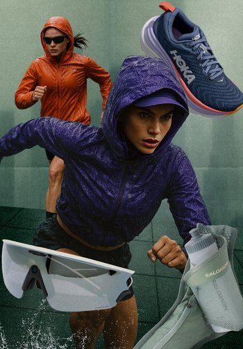 Chaquetas con capucha en naranja y púrpura, zapatillas de correr en azul marino, gafas de sol transparentes y una mochila de hidratación verde sobre un pavimento mojado.