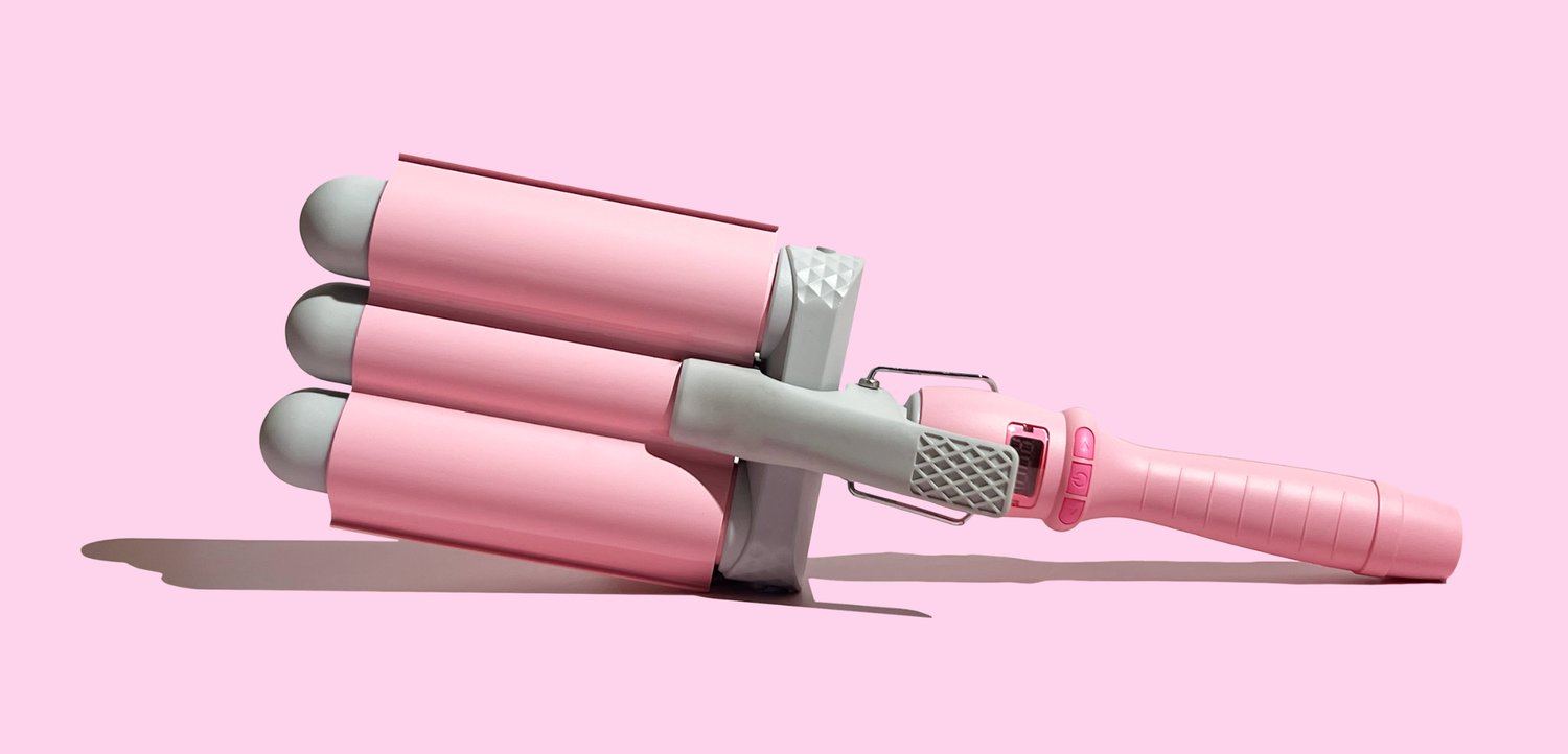 Fer à friser à trois cylindres rose et gris avec une poignée rose sur un fond rose clair.