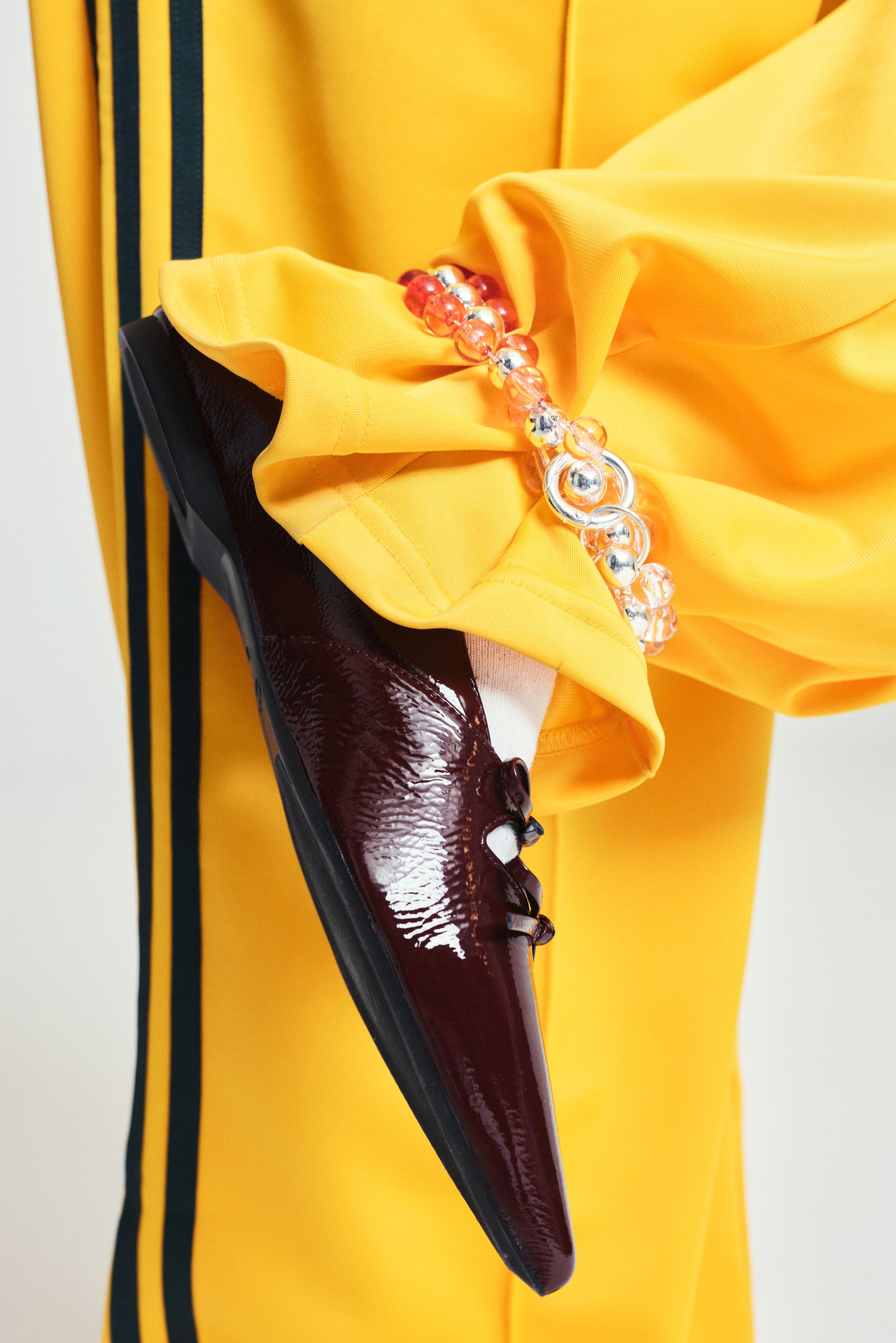 Un primo piano di una scarpa bordeaux lucida con lacci, abbinata a pantaloni gialli, accentuata da colorate perline di plastica sul tessuto.