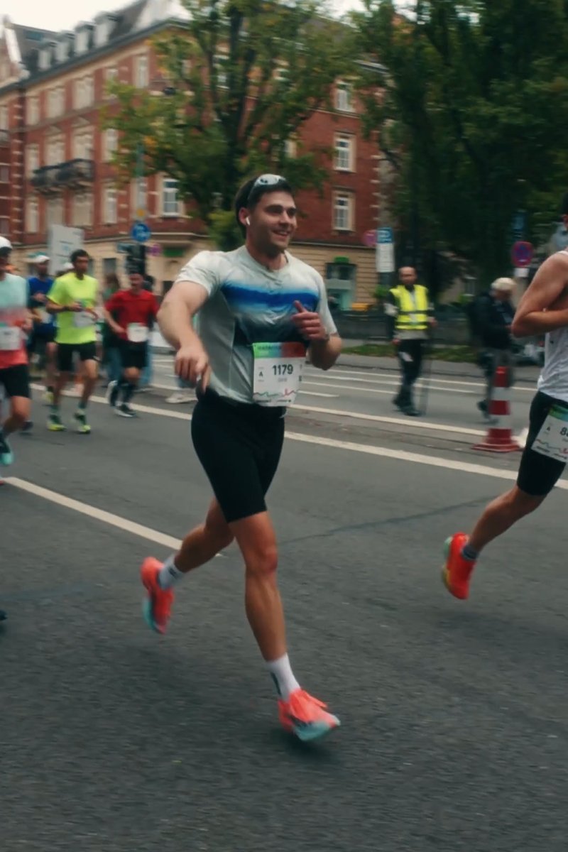 Läufer trägt ein hellgraues Shirt mit blauem Farbverlauf, schwarze Shorts und knallpinke Laufschuhe, nimmt an einem Marathon teil.