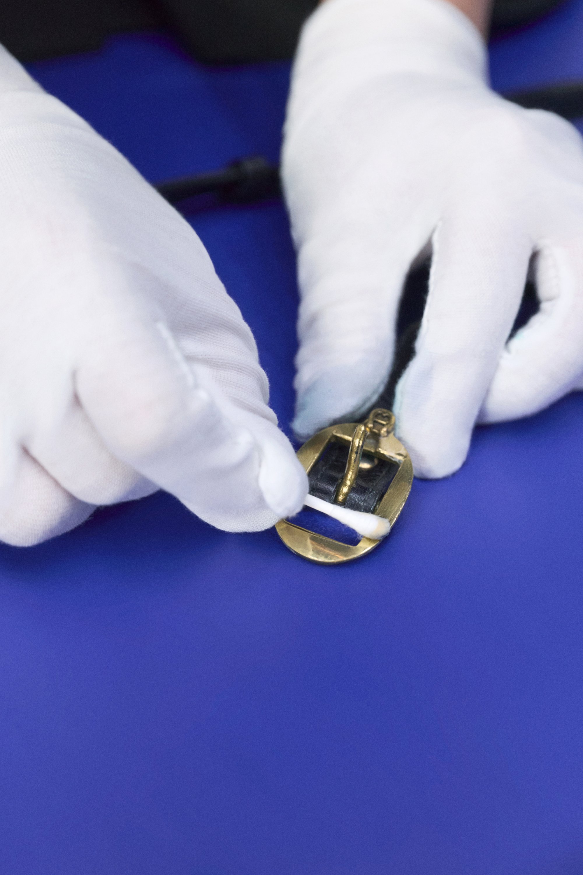Due mani guantate posizionano con attenzione una fibbia color oro su un cinturino nero, su uno sfondo blu.