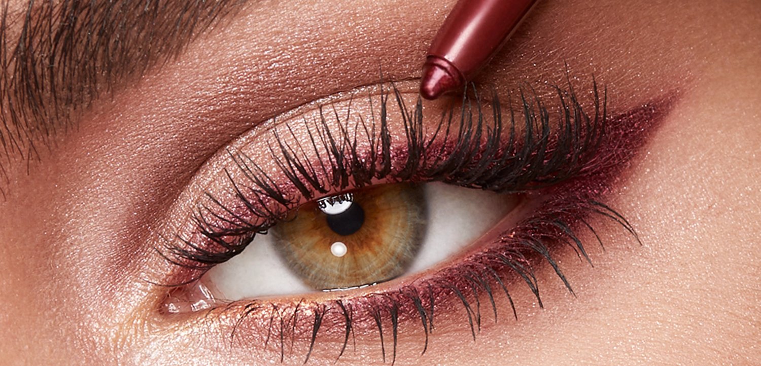 Gros plan d’un œil marron avec de longs cils, appliquant un eye-liner rose foncé sur la paupière supérieure.