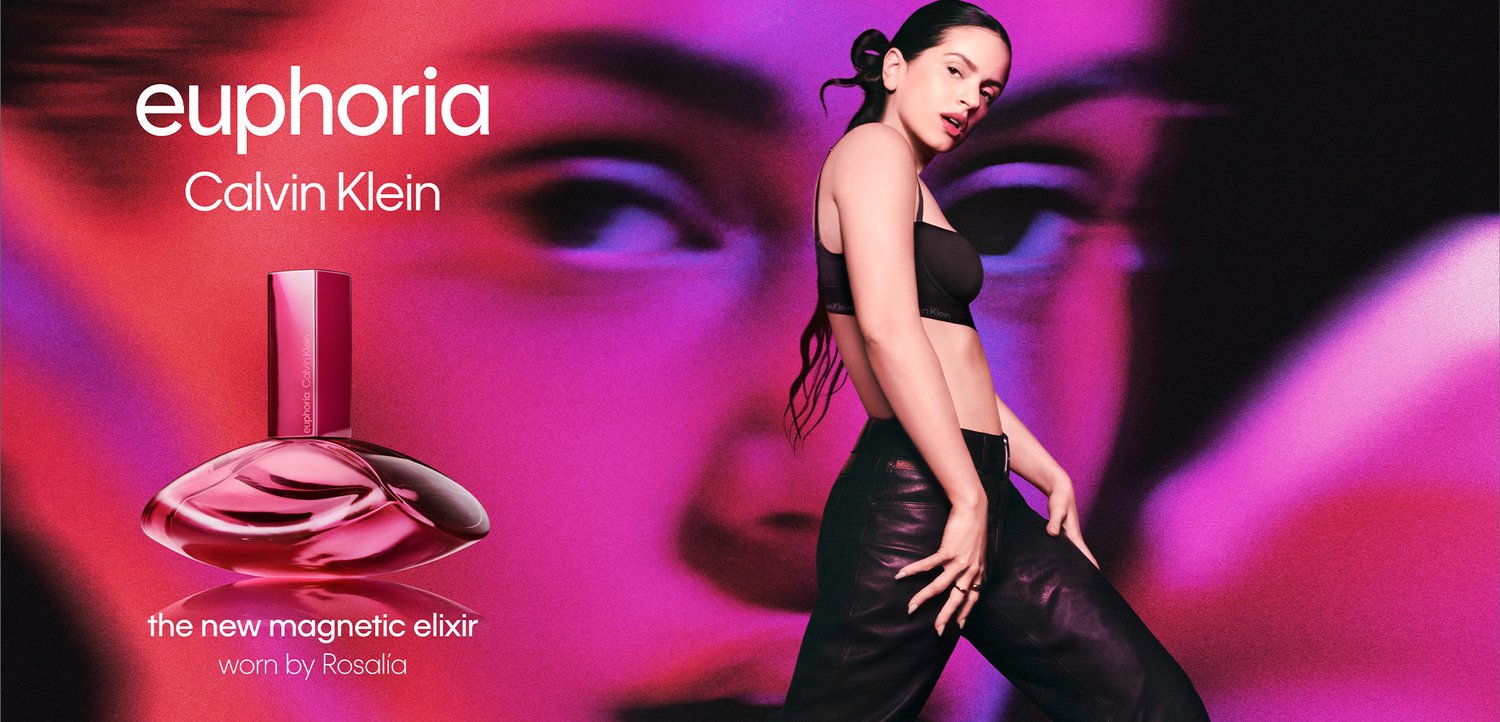 Rosalía i sort outfit poserer selvsikkert ved siden af en stor Calvin Klein Euphoria parfume flaske med en levende lilla og rød baggrund.