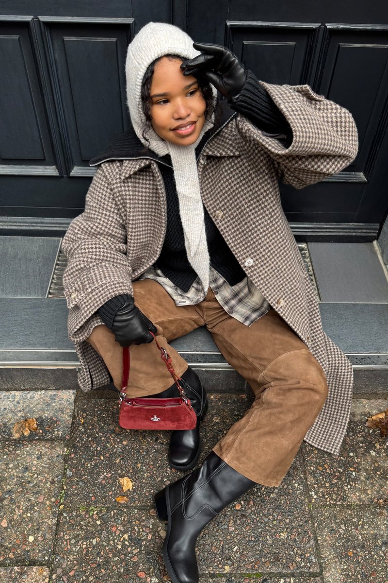 Brun hundetandsmønstret frakke, cremefarvet strikket hættetrøje, sorte handsker og brune ruskindsbukser. Sorte støvler med hæl og rød håndtaske med sølvhardware.