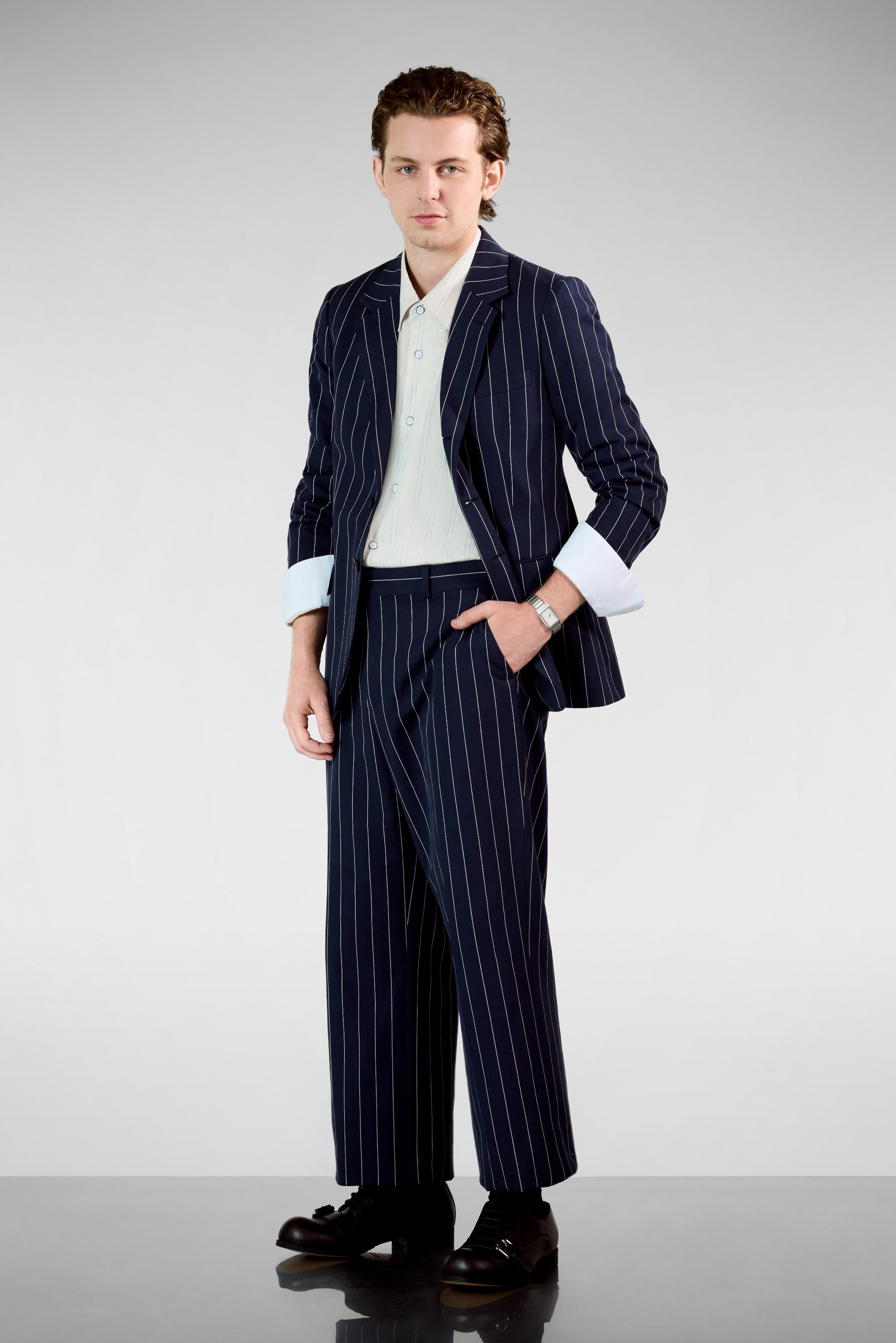 Traje a rayas navy con chaqueta ajustada y pantalones de pierna ancha, combinado con una camisa de botones de color claro y zapatos negros.