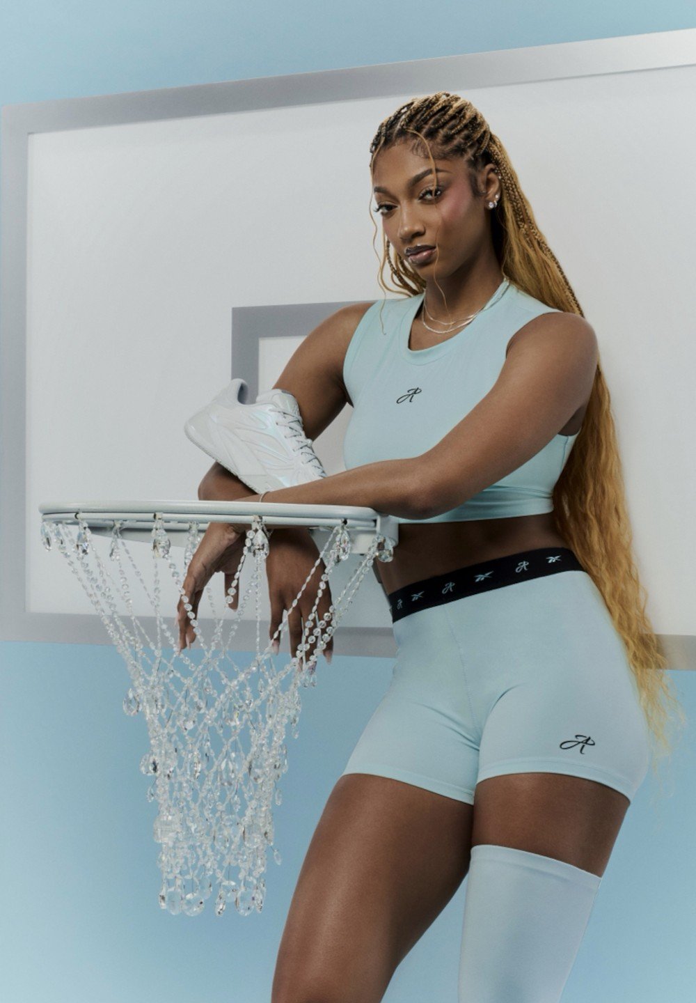 Naine helesinises spordirõivastuses ja pikkade palmikutega, toetumas kristallvõrguga korvpallivõrgu peale, hoides valget tossu.