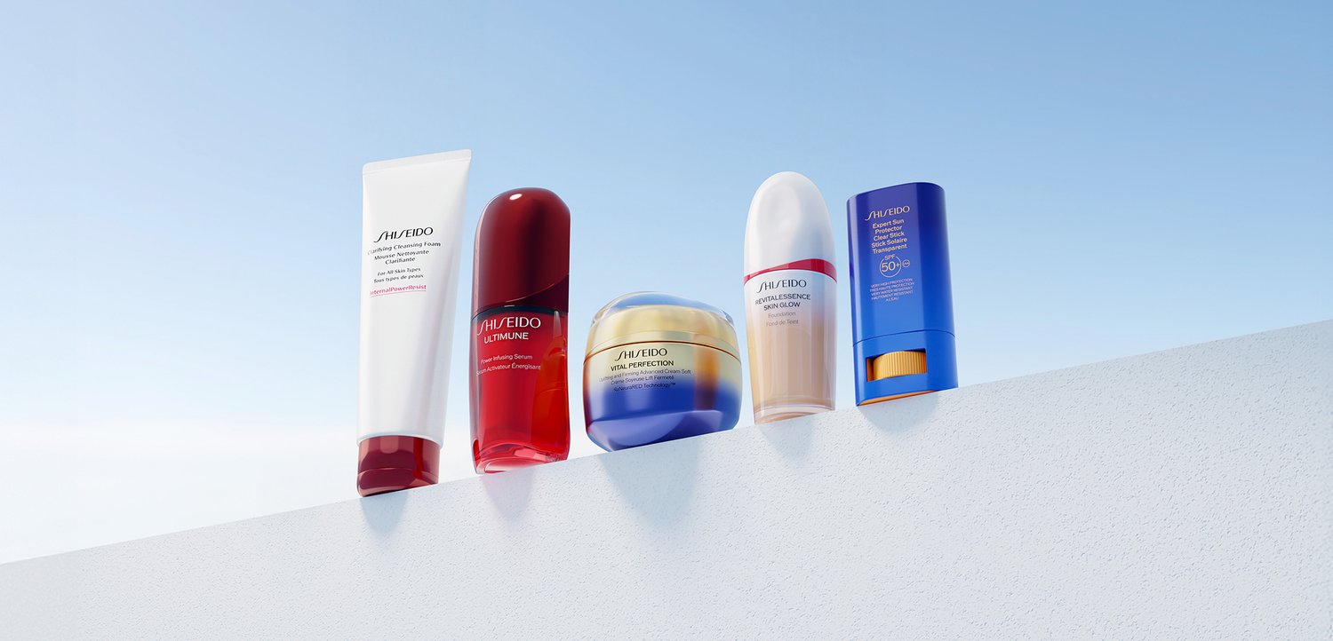 Pięć produktów do pielęgnacji skóry Shiseido w białych, czerwonych, złoto-niebieskich, białych i niebieskich opakowaniach, ustawionych na białej powierzchni na tle przejrzystego nieba.