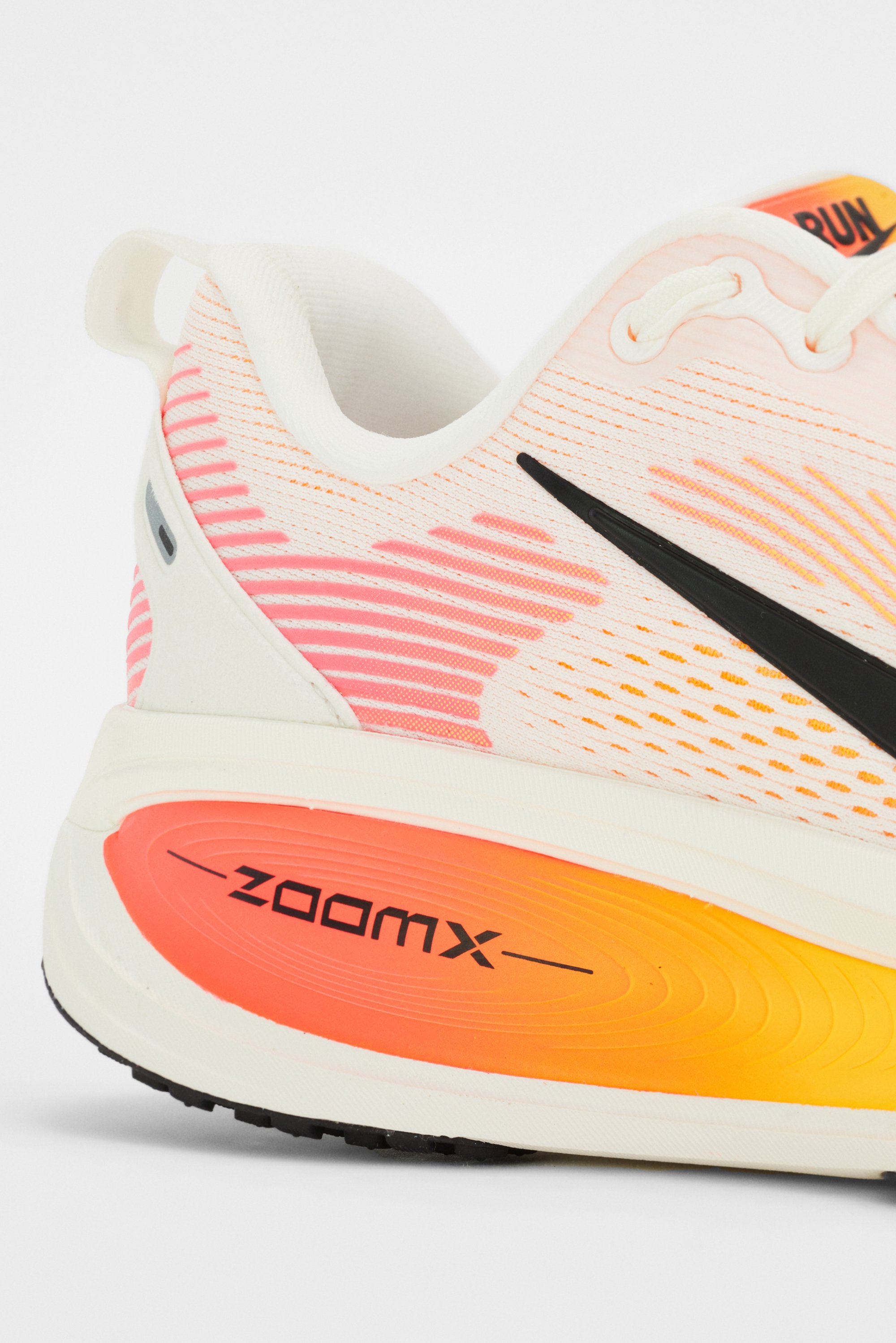 Close-up of a lightweight running shoe featuring a white and pink upper, black swoosh logo, and an orange-to-yellow gradient midsole labeled "ZOOMX."
