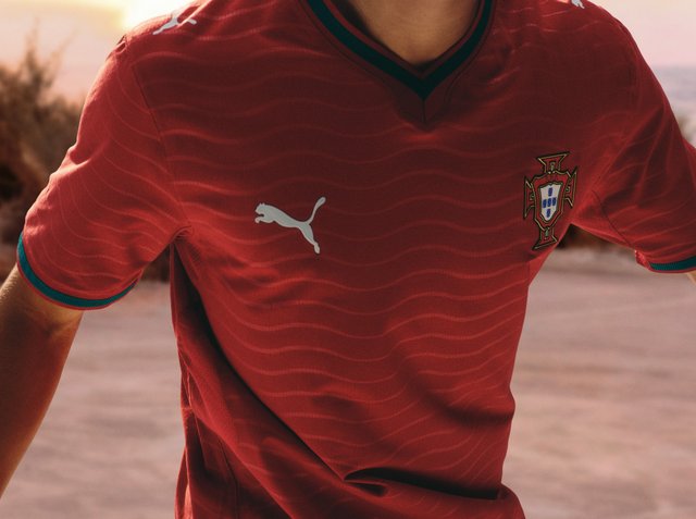 Person, die ein rotes Portugal-Fußballtrikot mit Puma-Logo und Mannschaftswappen trägt, aufgenommen von den Schultern bis zur Taille.