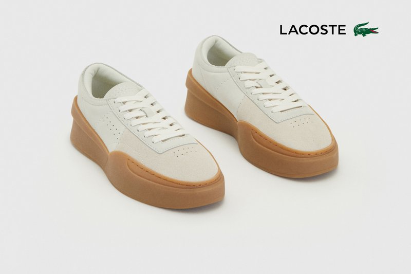 Baskets en daim et cuir blanc avec une semelle en caoutchouc beige, présentant des détails perforés et des lacets blancs plats.