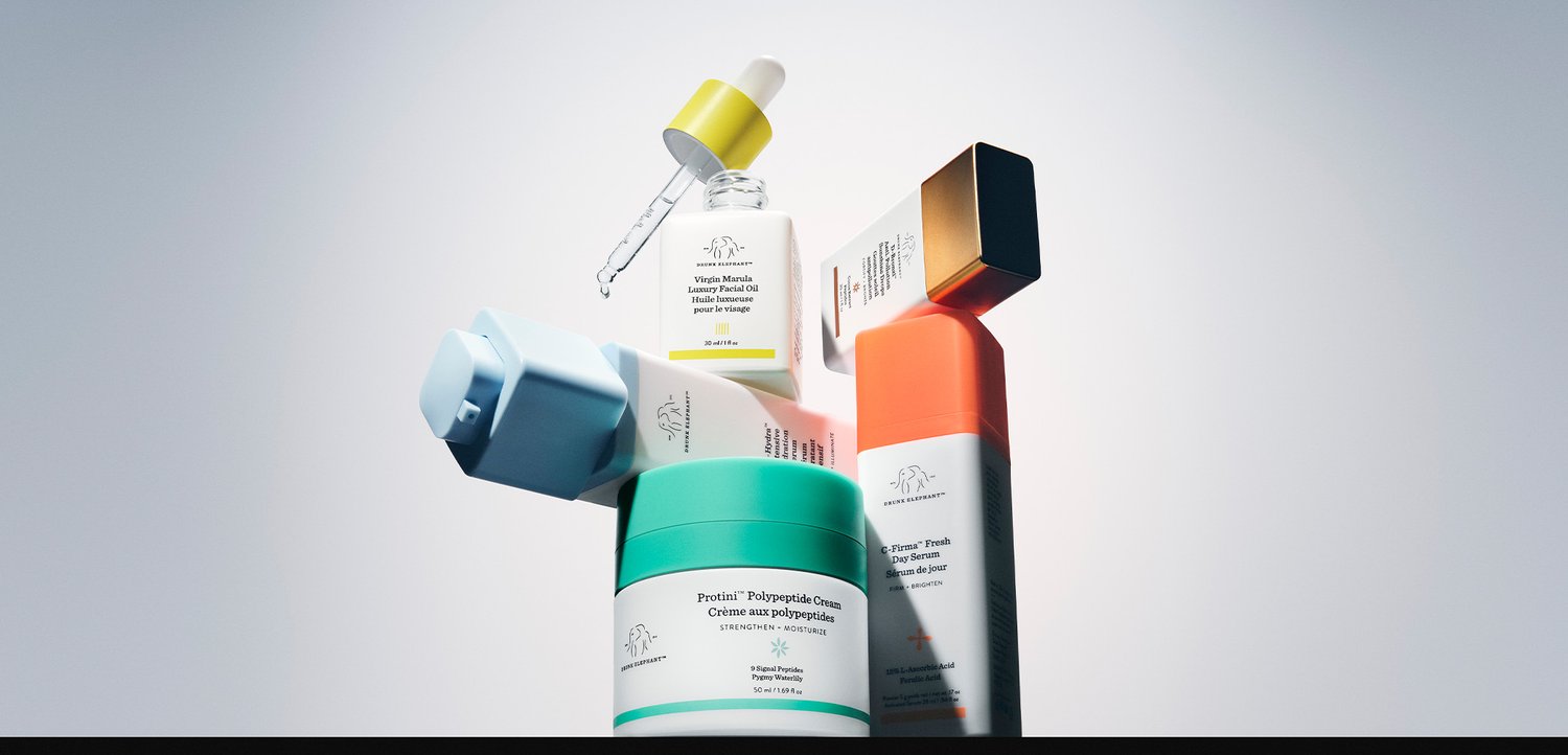Various skincare products including a jar of cream, a facial oil with dropper, and several boxed serums arranged on a light background.