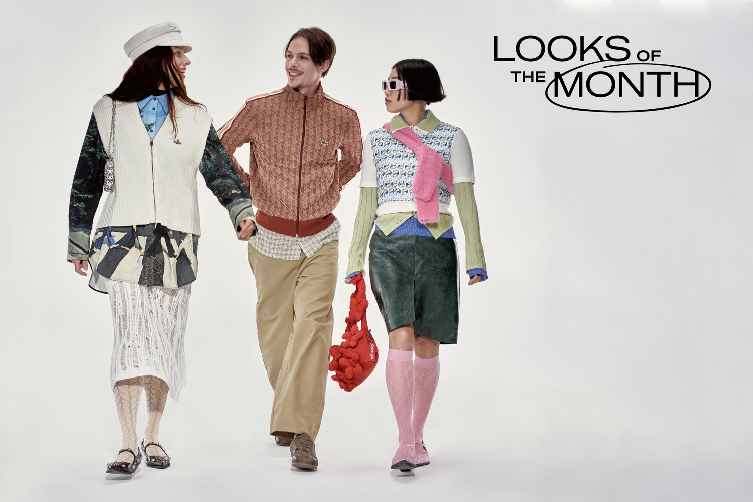 Tres modelos caminan juntas, mostrando estilos de moda diversos. Una lleva un sombrero y otra lleva un bolso rojo, sonriendo ante un fondo sencillo.