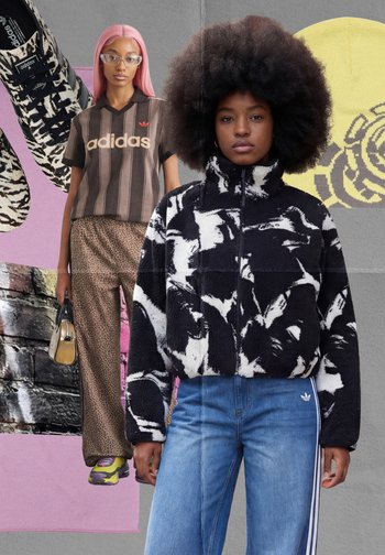 Twee vrouwen die Adidas-kleding dragen: de ene in een zwart-wit fleece met patroon en jeans, de andere in een Adidas-shirt, luipaardbroek, roze haar en sneakers.