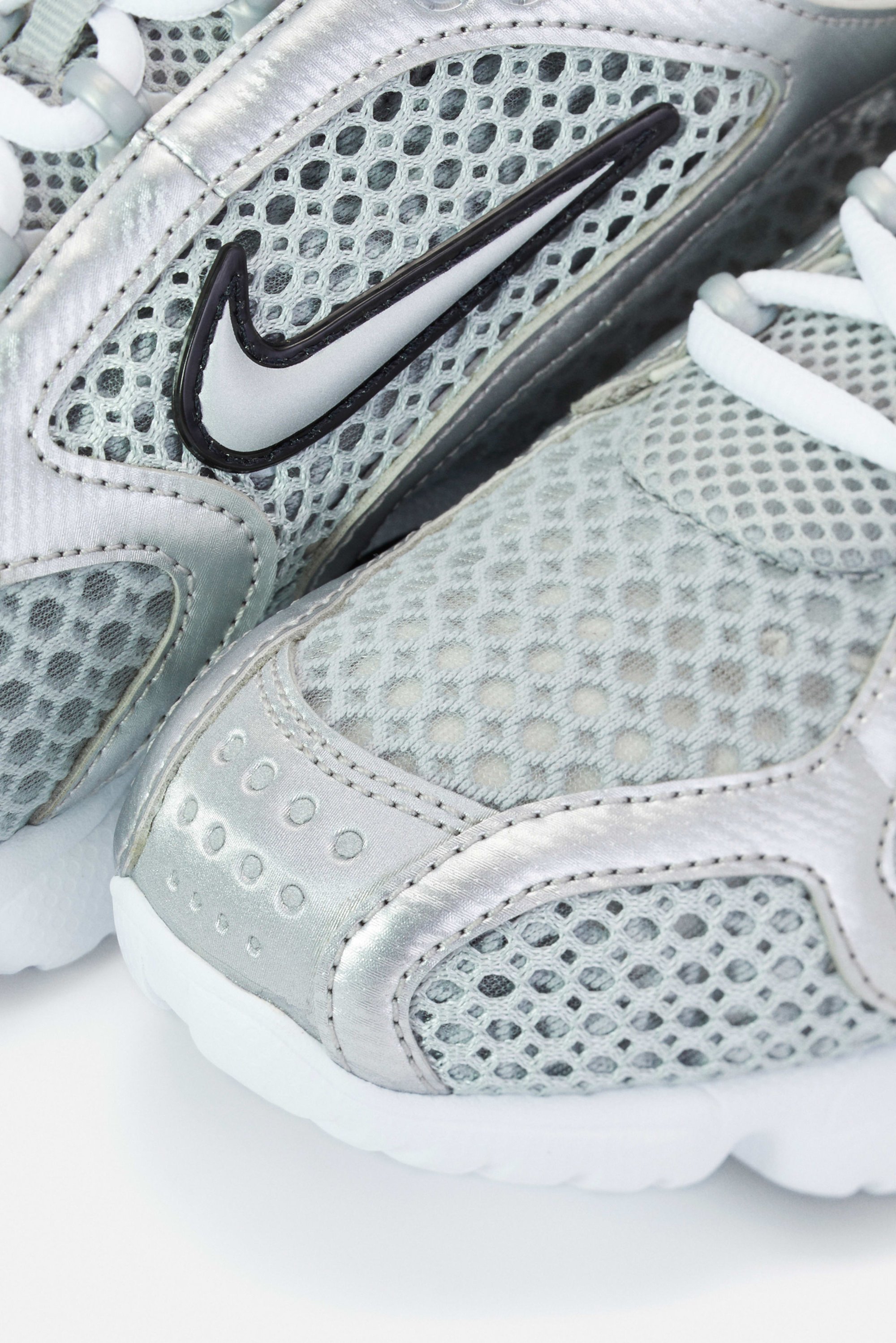 Close-up van zilveren Nike sport schoenen met een mesh ontwerp, zwart logo en witte veters, waarbij de textuur en details van het schoeisel worden benadrukt.