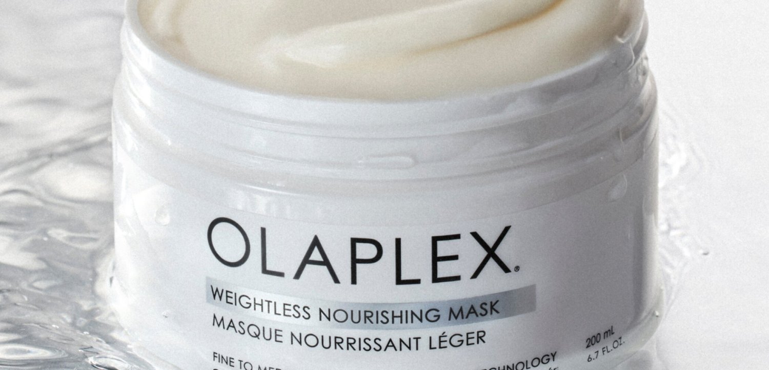 Open pot van Olaplex Weightless Nourishing Mask, waarin een gladde witte crème zichtbaar is, geplaatst op een nat oppervlak.