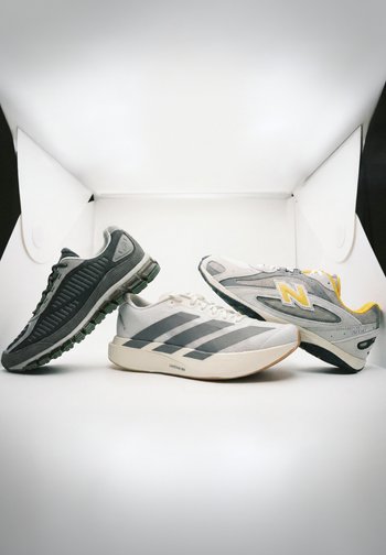 Trois paires de chaussures de sport : grises avec un design texturé, crème avec trois rayures foncées, et argentées/grises avec des accents jaunes.