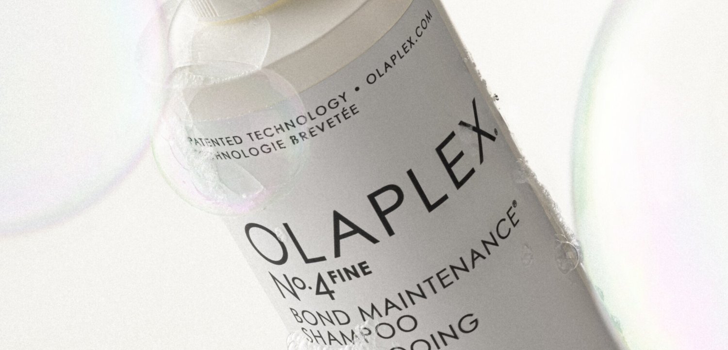 Primo piano di una bottiglia di shampoo Olaplex No.4 Fine Bond Maintenance con bolle su sfondo bianco.