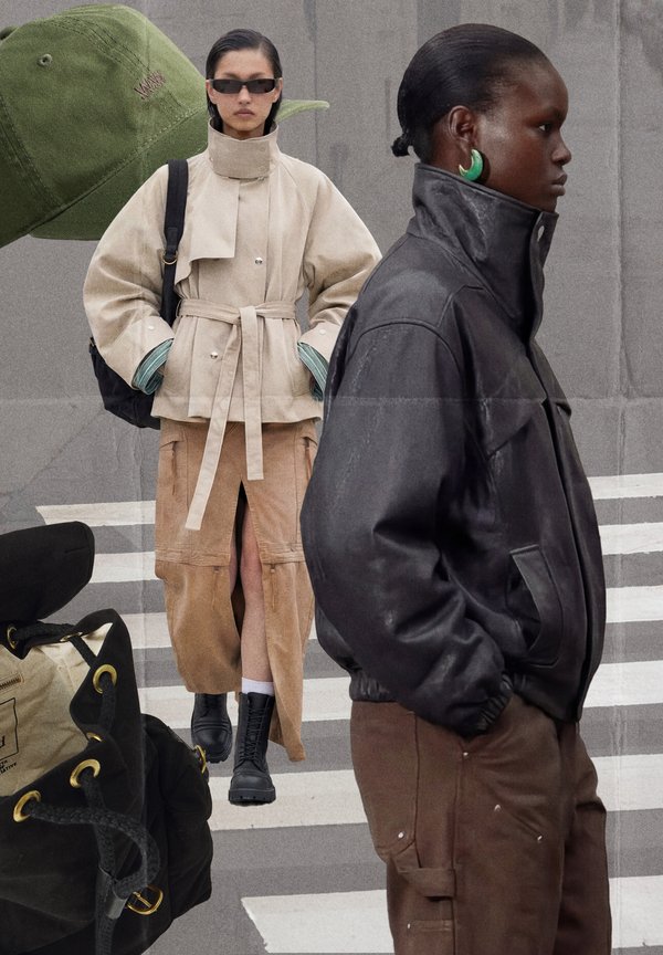 To modeller iført oversized jakker og cargobukser, den ene i beige og den anden i sort, poserer med tasker og en grøn kasket i baggrunden.