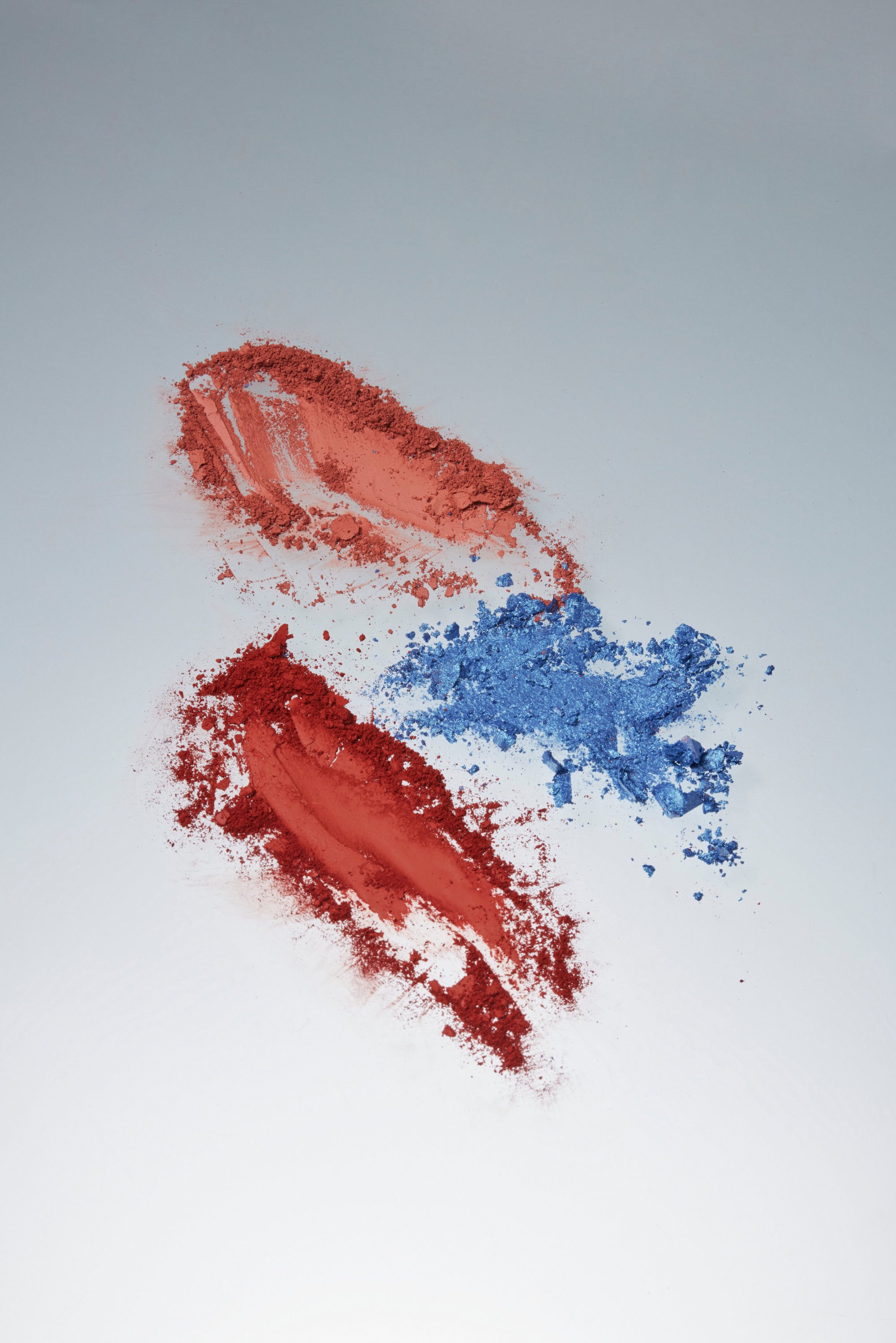 Red and blue powdered pigments spread across a white surface, creating a vibrant contrast with distinct textures and shapes.