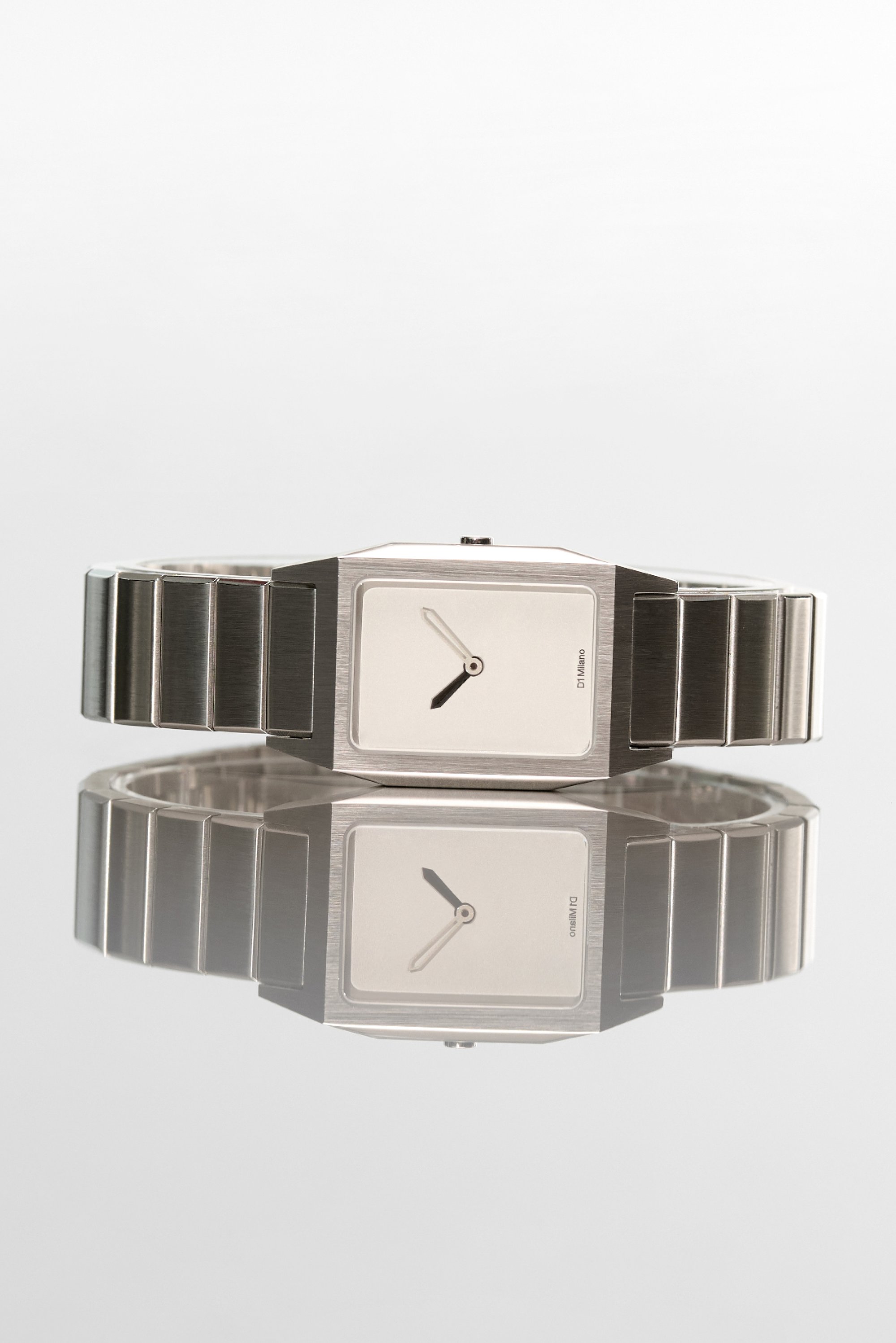 Reloj de acero inoxidable plateado con una esfera rectangular, diseño minimalista, esfera blanca, manecillas negras y una pulsera de metal con eslabones.