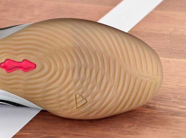 Cipőtalp színt nem hagyó gumiból, hullámos tapadómintával és kis piros tapadórészlettel, fából készült padlón, fehér vonal közelében.