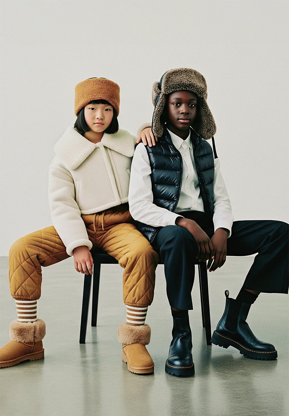 Kaks last istuvad toolil. Üks kannab valget karvase voodriga jopet ja pruunide karvadega kaunistatud kübarat; teine musta vestiga ja halli kübaraga. Pruunid püksid ja karvadega ääristatud saapad.