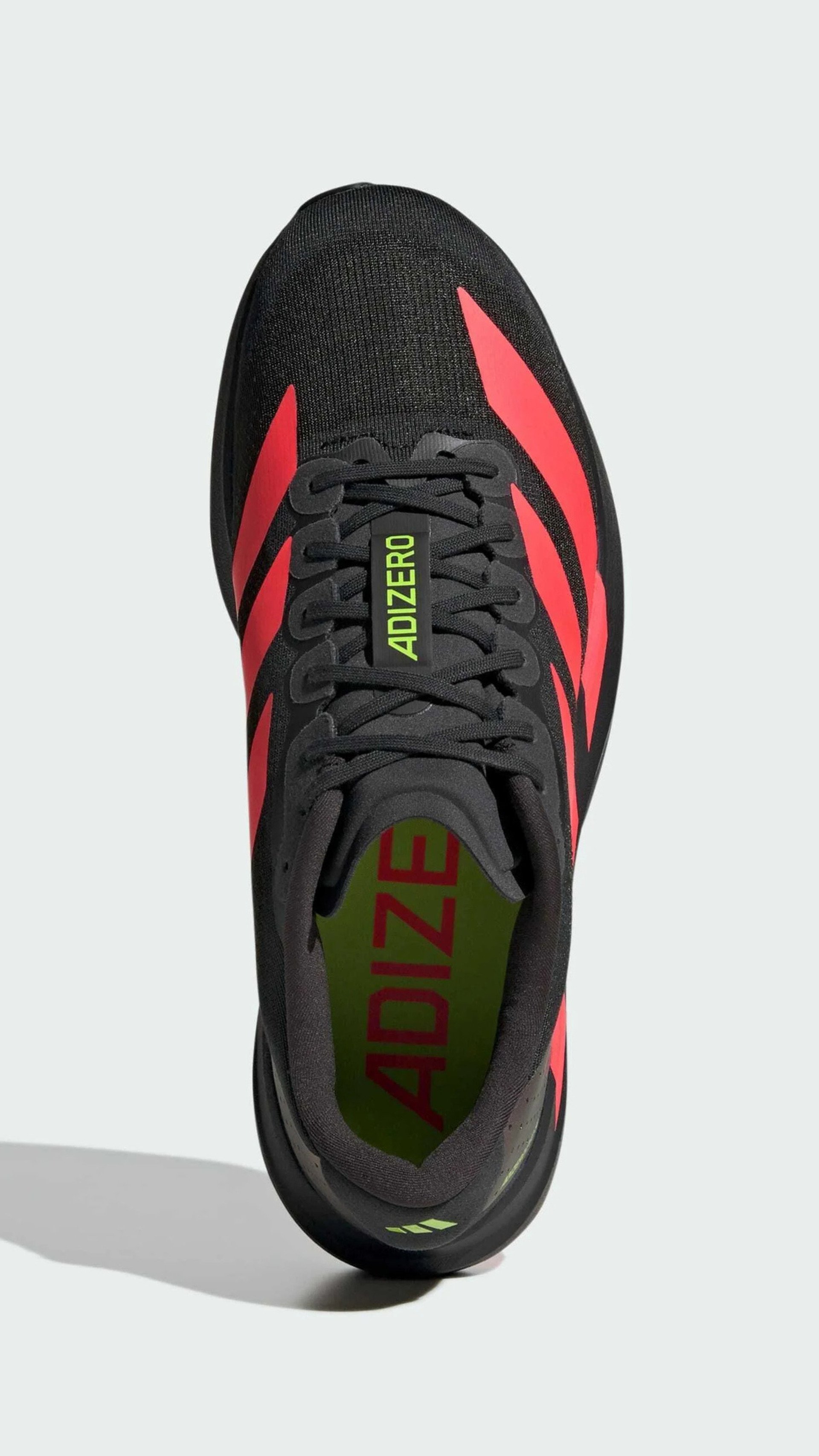 Zapato deportivo negro con rayas rojas y acentos verdes, que presenta la etiqueta "ADIZERO" en la lengüeta y un diseño elegante y moderno.