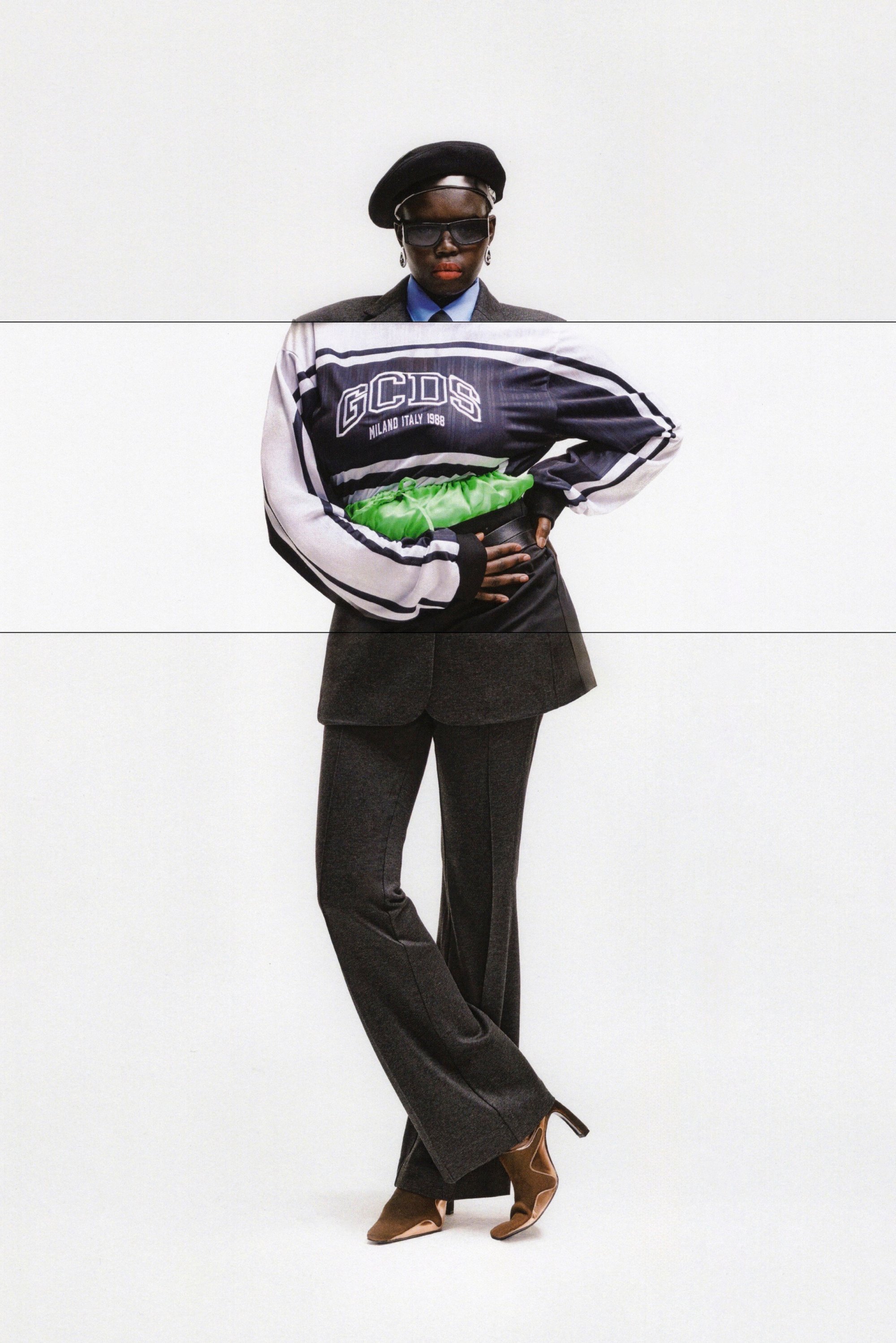 A person wearing a stylish jacket with "GCDS" print and a beret poses confidently, holding a green accessory against a plain background.