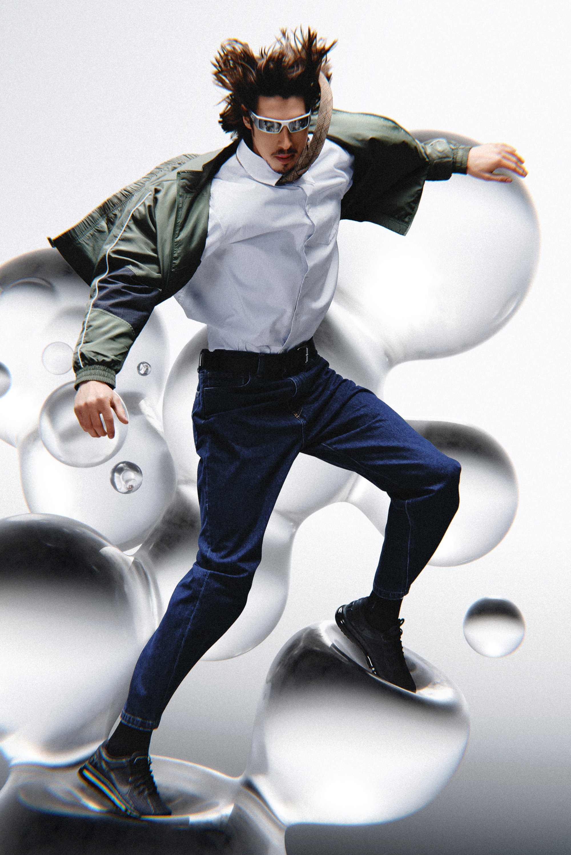 A person with tousled hair wears sunglasses and a jacket, balancing on abstract liquid shapes with a dynamic pose against a light background.