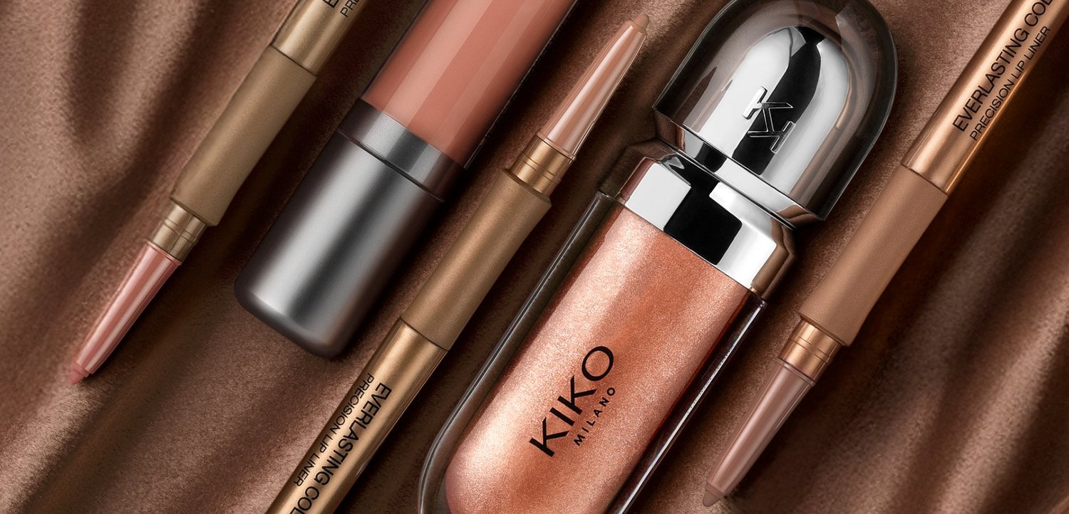 Verschiedene KIKO Milano Make-up-Produkte in Roségold- und Nude-Tönen, arrangiert auf einem braunen Satin-Stoffhintergrund.