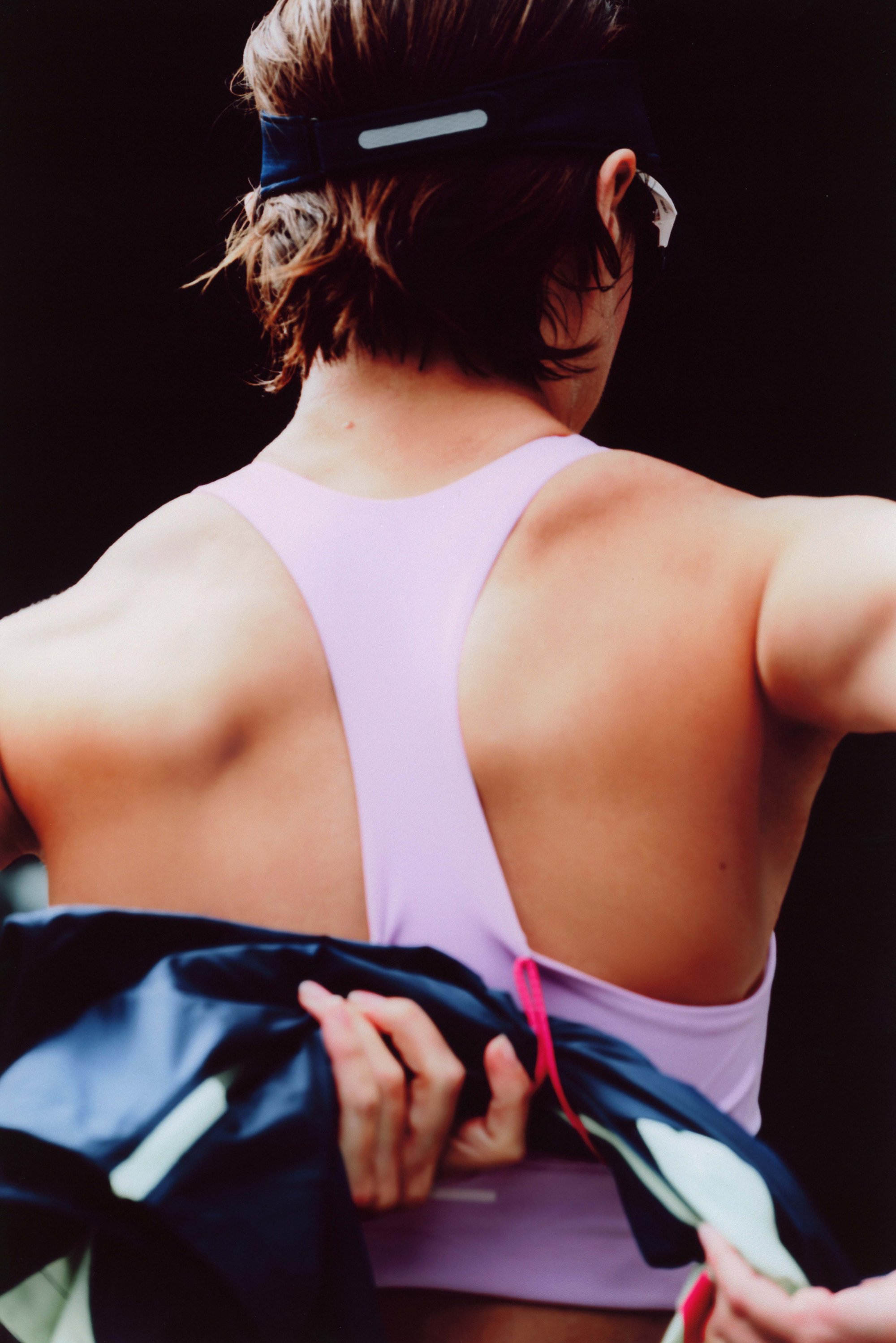 Purple athletic tank top featuring a low back design, secured with dark navy fabric. Textured straps and accentuated hardware detail.