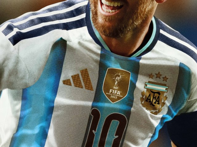 Männlicher Fußballspieler, der Argentiniens blau-weiß gestreiftes Trikot mit FIFA 2022 Weltmeister-Abzeichen und der Nummer 10 trägt, lächelt und feiert.