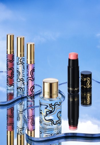 Three lip gloss tubes, a perfume bottle, and a pink cream stick with cap on reflective blue surface and sky background.