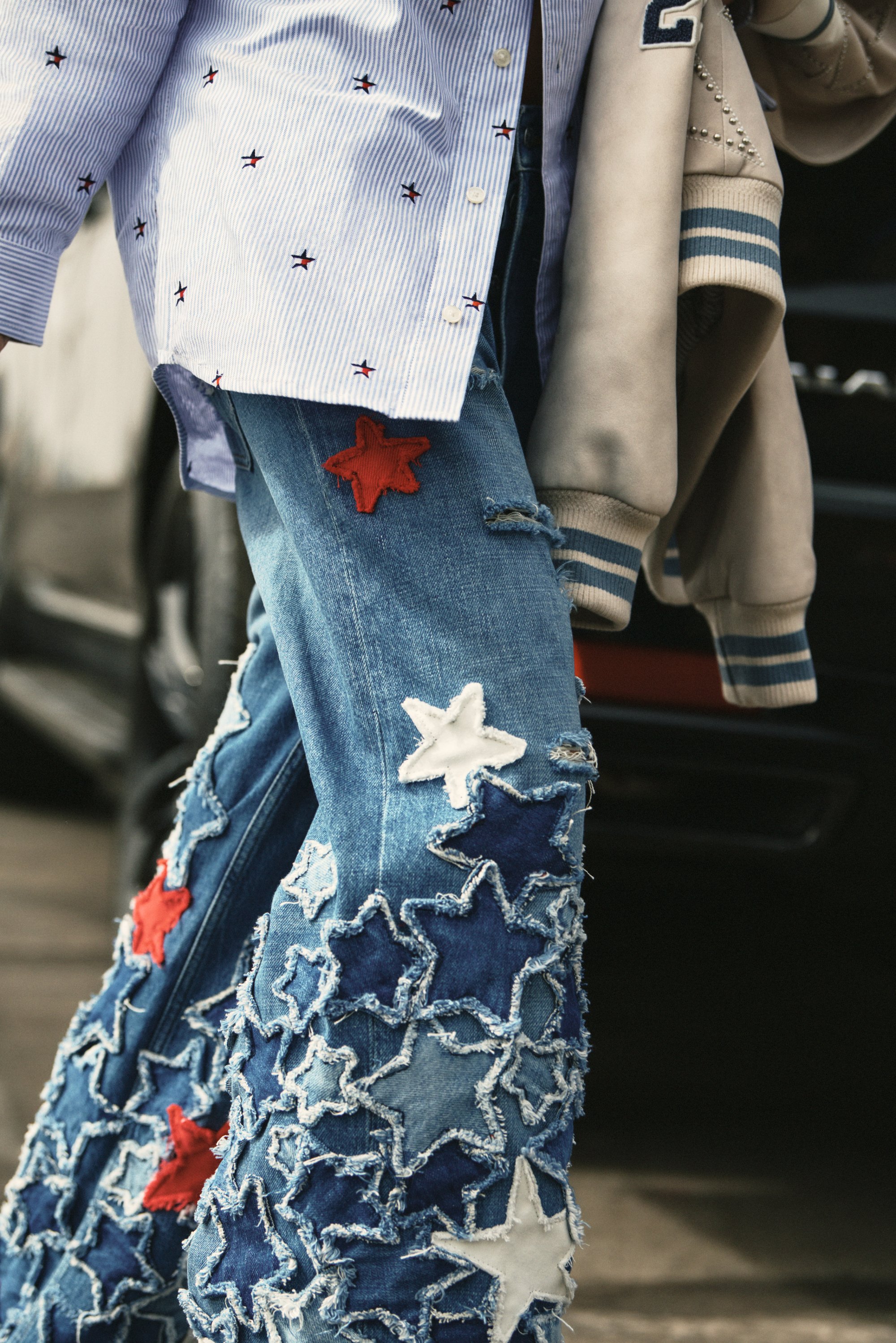Blue denim jeans with star patches in red, white, and blue, paired with a striped shirt, stand out against a dark car background.