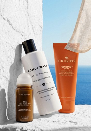 Drei Hautpflegeprodukte, darunter Junglück Zinc Deodorant Roll-on, Bondi Wash After Sun Gel und Origins GinZing SPF 40 Feuchtigkeitscreme, an einer weißen Wand.