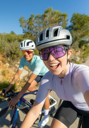 Deux cyclistes portant des casques et des lunettes de soleil roulent en plein air par une journée ensoleillée, souriant et appréciant une sortie à vélo sur route.