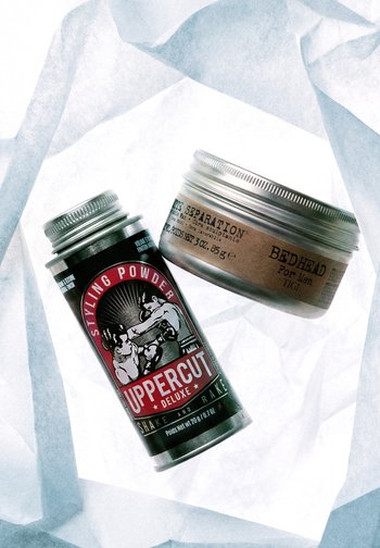 Uppercut Deluxe Styling-Puderdose und Bed Head for Men Haarmodellierpaste-Glas auf einer hellen, strukturierten Oberfläche.