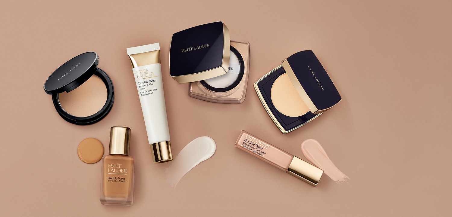 Verschiedene Estee Lauder Double Wear Foundation-Produkte mit Farbmuster auf beigem Hintergrund, darunter flüssige, cremige und Puder-Formulierungen.