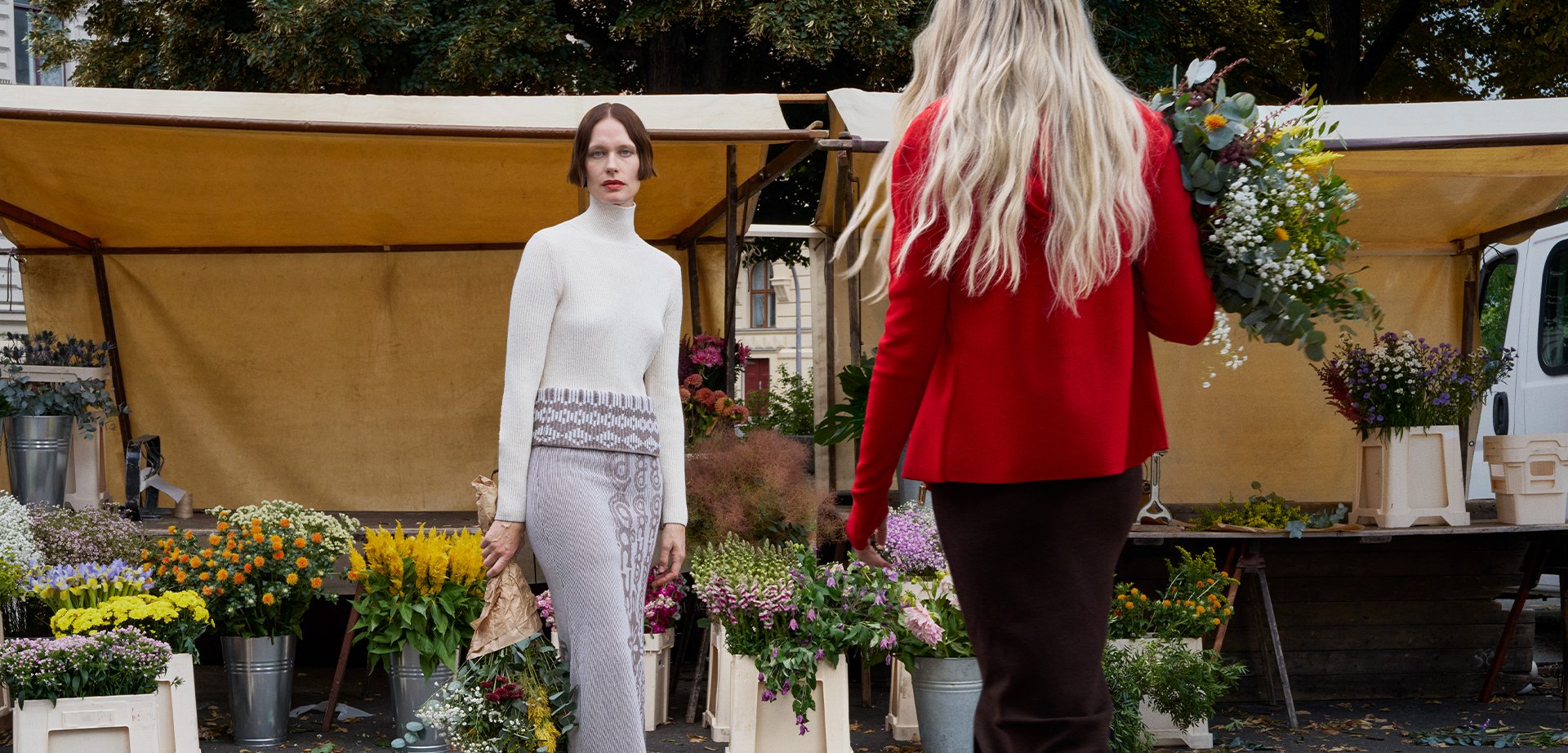 White knitted turtleneck sweater paired with a patterned grey skirt. Flower market filled with vibrant blooms in pots. Soft textures and natural materials.