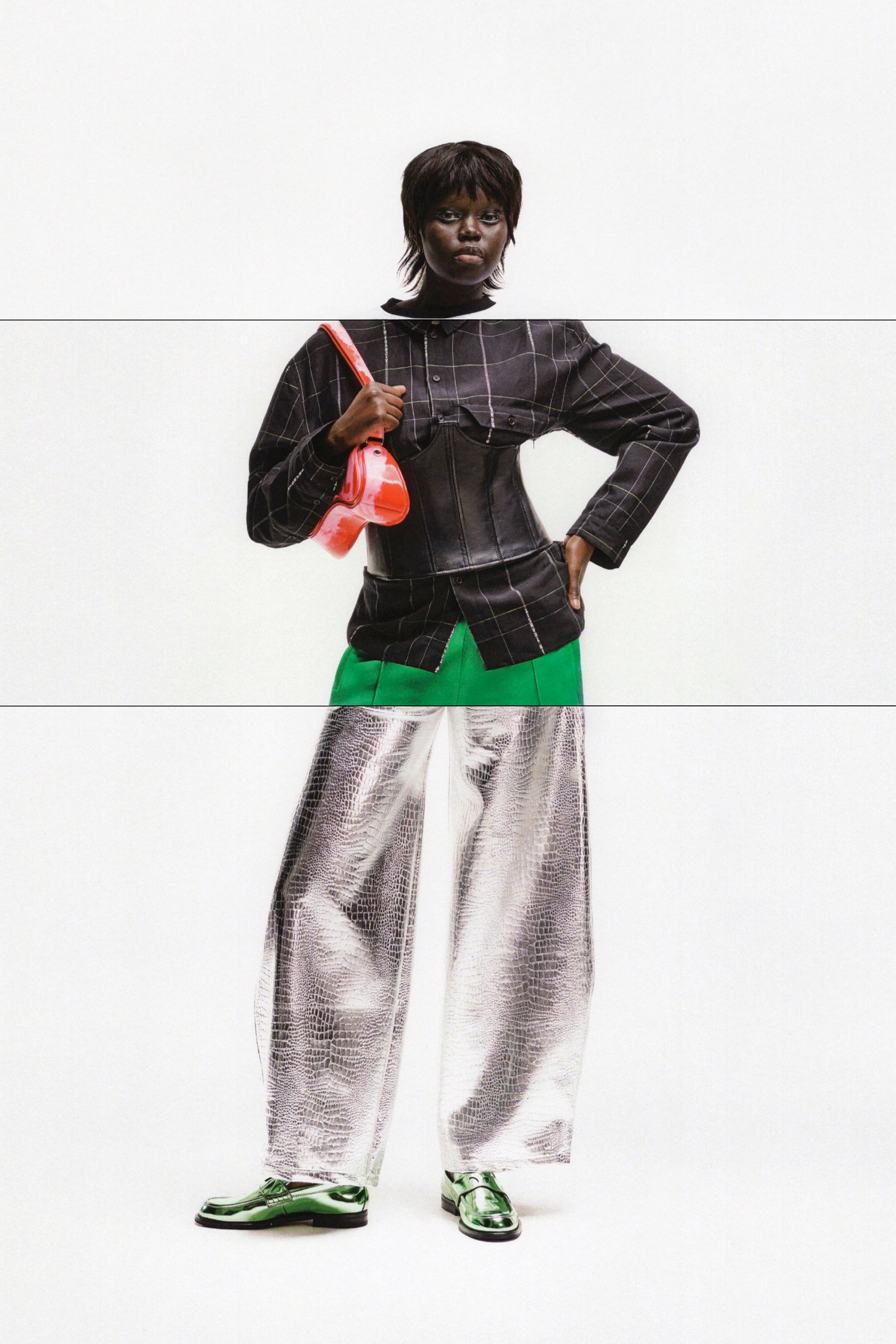 Model poses with confidence, wearing a black checked top, green skirt, reflective silver wide-leg pants, and shiny green shoes, holding a red bag.