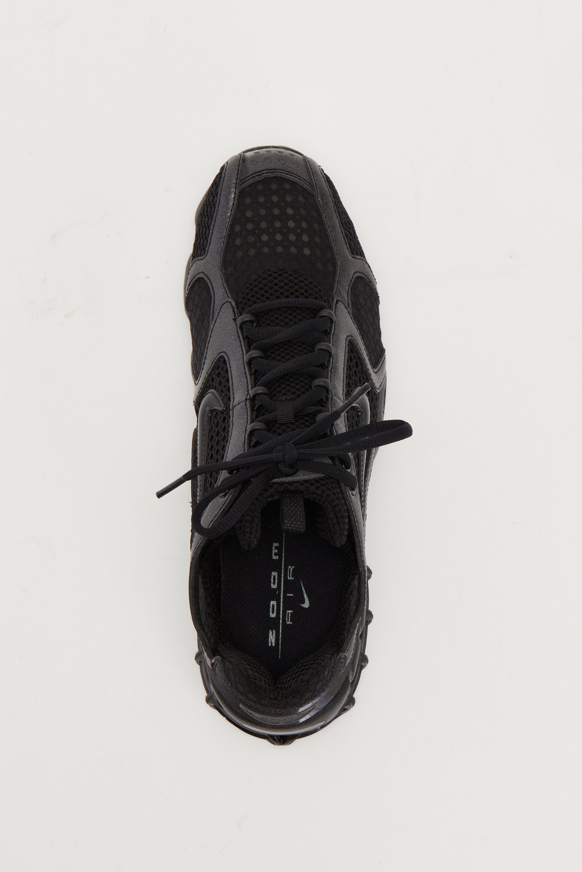 Black athletic shoe with mesh panels, laces, and a textured sole, viewed from above against a white background. Logo visible inside.