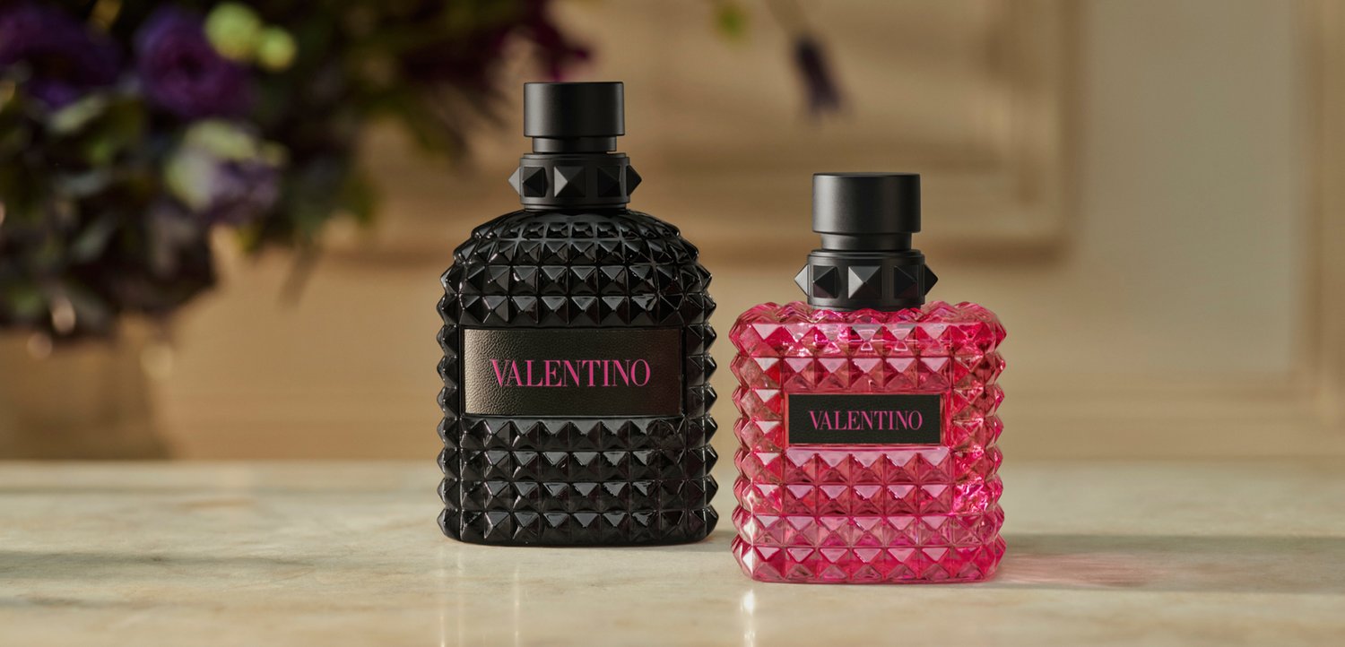 Two Valentino studded perfume bottles, one black and one pink, placed side by side on a marble surface.