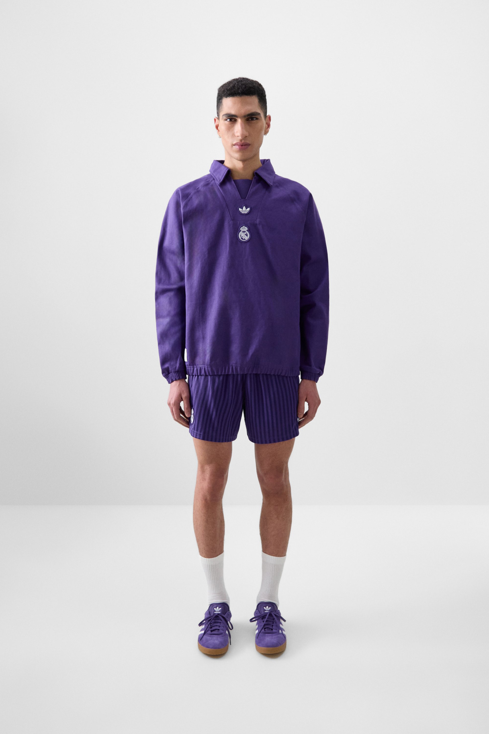 Een mannelijke model staat tegen een effen achtergrond, gekleed in paarse sportkleding met een groot logo en bijpassende schoenen, wat een sportieve uitstraling geeft.