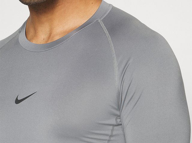 Man draagt een nauwsluitend grijs Nike sportshirt met zichtbare naden en een zwart swoosh-logo op de borst.