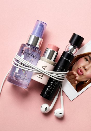 Sérum capillaire Kérastase, stick ILIA, spray MAC, écouteurs blancs et photo d'une femme envoyant un baiser sur fond rose, écouteurs enroulés autour des produits.