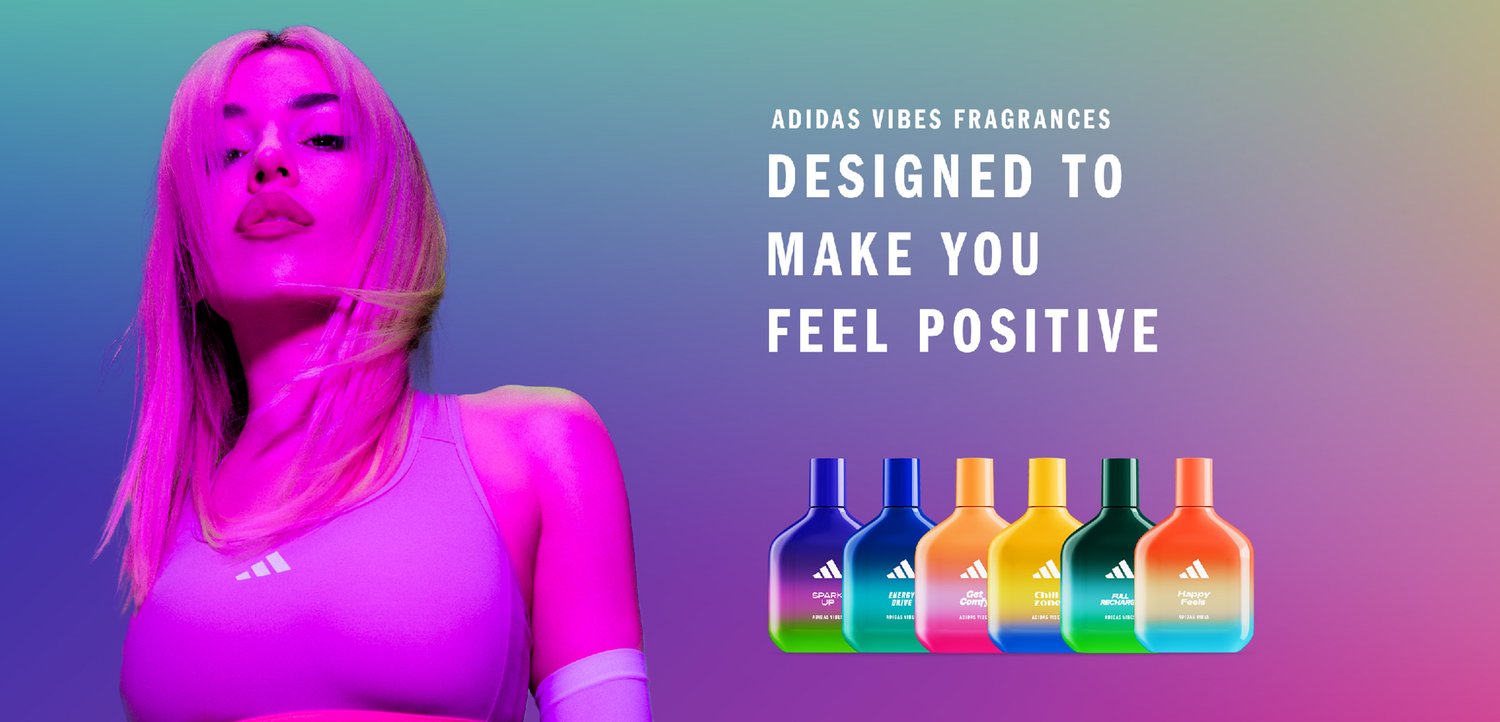 A woman with long, pink hair poses confidently, alongside colorful Adidas fragrance bottles against a gradient background with the slogan, "Designed to Make You Feel Positive."