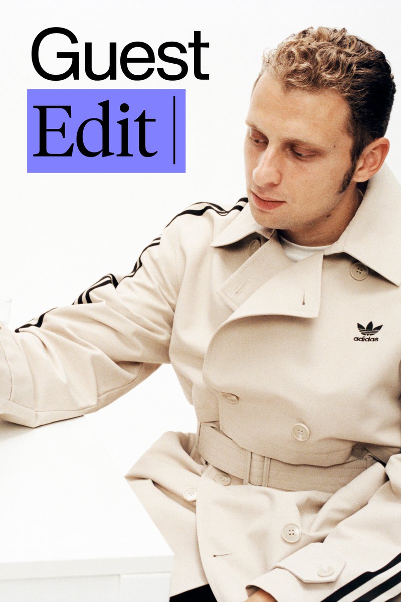 Een man in een beige trenchcoat met zwarte strepen richt zich op een witte ondergrond, met de tekst "Gast Bewerking" prominent in beeld.