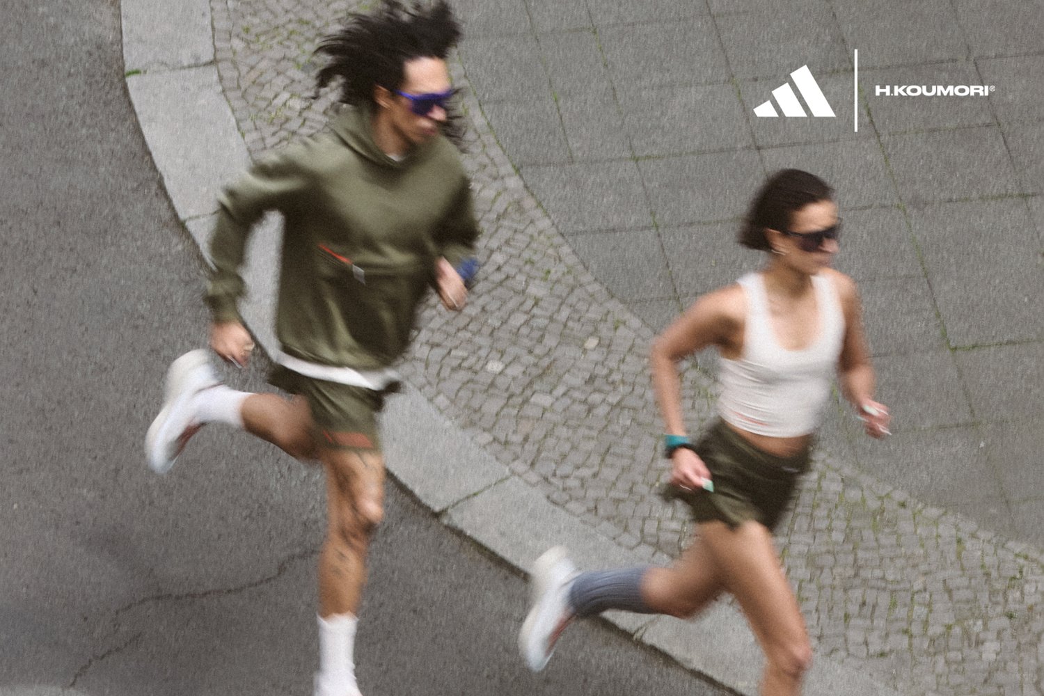 Due persone in abbigliamento sportivo corrono lungo una strada curvilinea. L'ambiente è urbano, con ciottoli e un'atmosfera dinamica e attiva.
