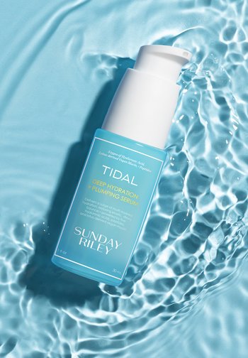 Bottiglia blu del siero Sunday Riley Tidal Deep Hydration and Plumping che galleggia in acqua limpida con riflessi di luce ondulati.